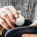 MiTag Duo Global Tracking Tag with PU Case (stock) - A white tracking tag is being placed into a navy blue pouch, held by a person with a knitted sweater.