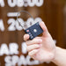 MiLock Duo Tag Luggage Lock - A black luggage lock with a keypad and a metal loop, held in a hand against a blurred background.