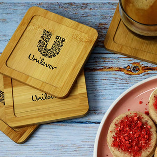 Aroma Coffee Coasters - A set of bamboo coasters featuring a logo, placed on a wooden table alongside a drink and cookies.