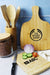 Tiga Bamboo Cutting Board - A bamboo cutting board with a handle, surrounded by kitchen utensils, sliced vegetables, and a glass container.