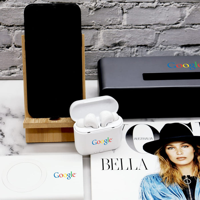Groove Bamboo Phone Stand - A bamboo phone stand with a smartphone, white earbuds case, and a magazine on a marble surface, featuring logos.