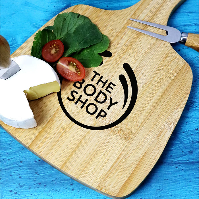 Artis Cheeseboard & Knife Set - A bamboo cheeseboard with a cheese wedge, cherry tomatoes, leafy greens, and a knife. Features a logo.