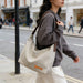 Dumpling Canvas Tote Bag - A beige canvas tote bag with brown straps, carried by a person in a grey sweater while walking on a city street.