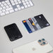 Wally Stand - A black card holder with multiple credit cards beside a smartphone and a white keyboard on a light surface.