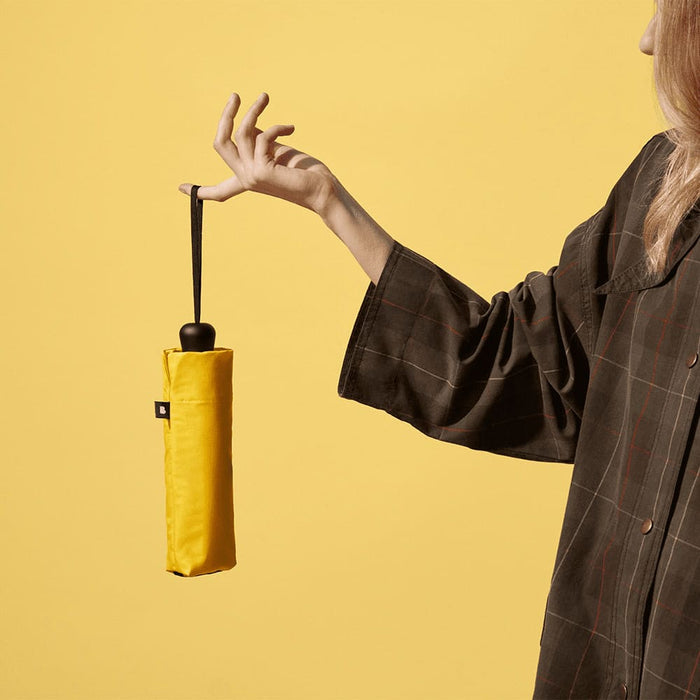 BLUNT Neo Umbrella - A yellow compact umbrella held by a person, with a plain background and a visible logo on the umbrella.