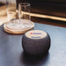 Boomer Bamboo Wireless Speaker - A wireless speaker with a bamboo top and a dark fabric body, featuring a logo on the top.