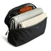 Bellroy Lite Packing Cube 6L - A black packing cube filled with a grey blanket, a beige item, and an orange accessory, featuring a mesh panel on top.
