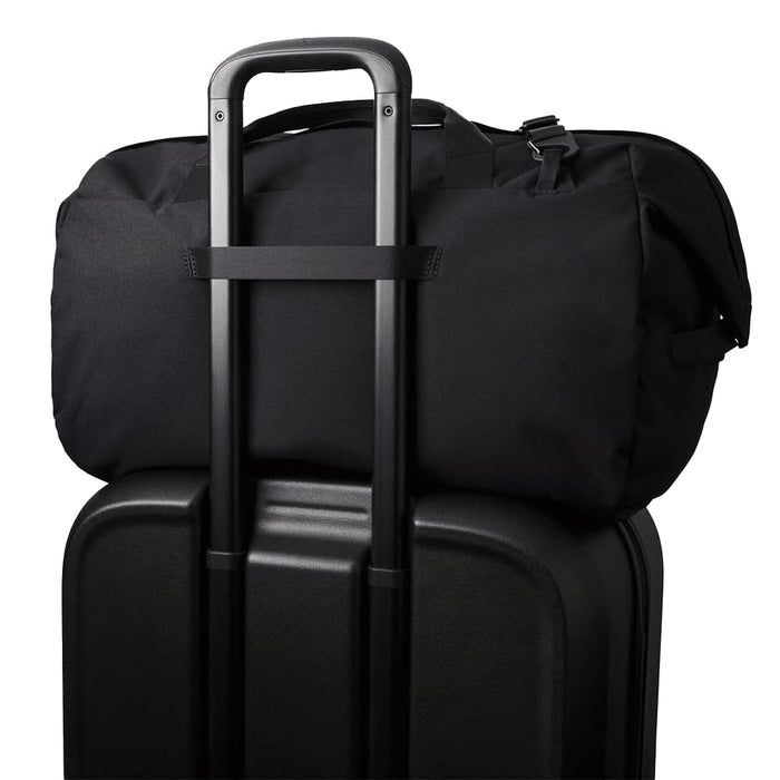 Bellroy Classic Duffel 45L - A black duffel bag sits on top of a black suitcase, featuring a trolley handle for easy transport.