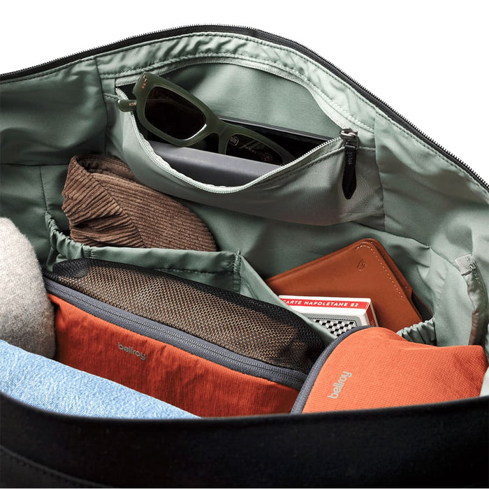 Bellroy Classic Duffel 45L - A black duffel bag interior featuring various items, including a pair of sunglasses, a notebook, and orange pouches.