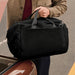 Bellroy Classic Duffel 45L - A black duffel bag with carrying handles is held by a person near a car trunk. The bag has a logo on it.