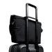 Bellroy Classic Messenger 13L - A black messenger bag positioned on top of a wheeled suitcase, featuring a retractable handle.
