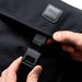 Bellroy Classic Messenger 13L - A black messenger bag with a flap and fastening mechanism, featuring a logo. A hand is holding the clasp.