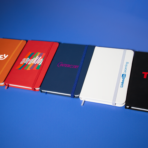 Minichroma A6 Notebook - A collection of A6 notebooks in red, navy blue, white, and black, featuring various logos and designs.