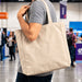 450gsm Victorian Canvas Tote Bag - A person holds a beige 450gsm Victorian canvas tote bag with shoulder straps. The bag features a logo.