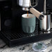 Carry Cup Olla Vacuum Coffee Cup w/ Ceramic Liner - 300ml - A drink bottle in a muted green colour with a ceramic liner, placed near an espresso machine on a black countertop.