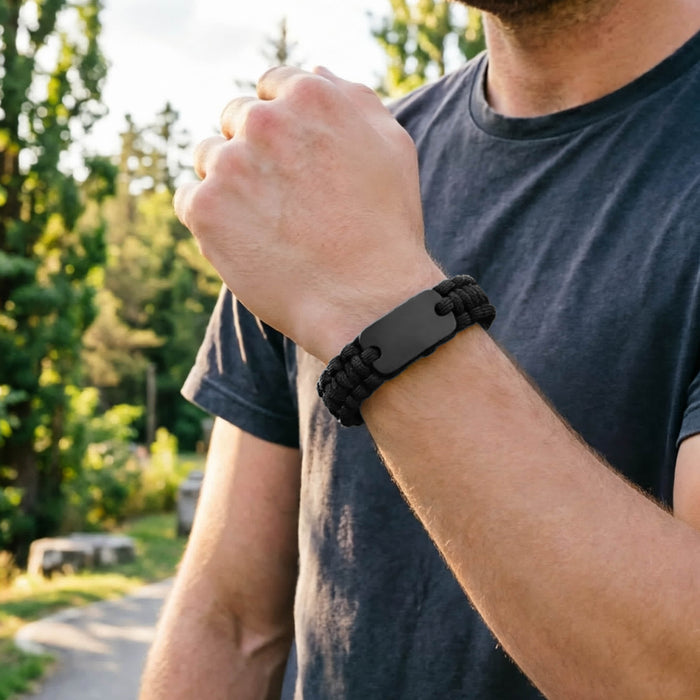 Paracord Bracelet with Metal Plate - A black paracord bracelet featuring a metal plate, worn on a wrist amidst a natural outdoor setting.