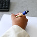 Harley Bamboo Spinner Pen - A bamboo spinner pen with a blue grip in a hand, resting on a lined notebook with a keyboard nearby.