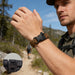 Paracord Bracelet With Whistle - A paracord bracelet in brown with a black clasp, worn by a man outdoors on a hiking trail. A close-up of the clasp is included.