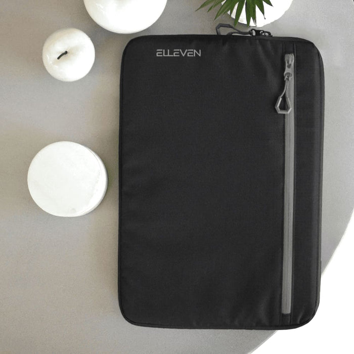 Work Essentials Pack - A black laptop sleeve featuring a front zipper pocket and a logo. Set against a neutral background with candles.