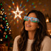 Paper Diffraction Glasses - Paper diffraction glasses in blue with festive designs, worn by a woman against a background of Christmas lights and decorations.