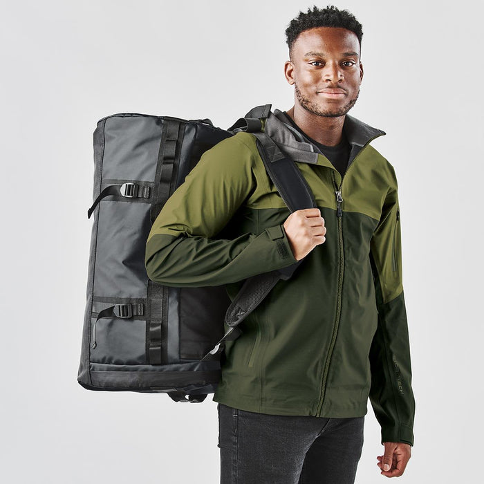 Nautilus Waterproof Duffle 70 - A man carrying a black and green Nautilus Waterproof Duffle 70 bag on his back, wearing a matching jacket.
