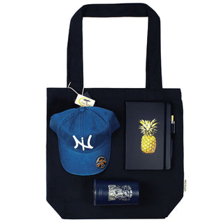 Lifestyle Essentials Pack - A navy tote bag holds a blue cap, a pineapple notebook, a pen, and a drink bottle, all featuring a logo.