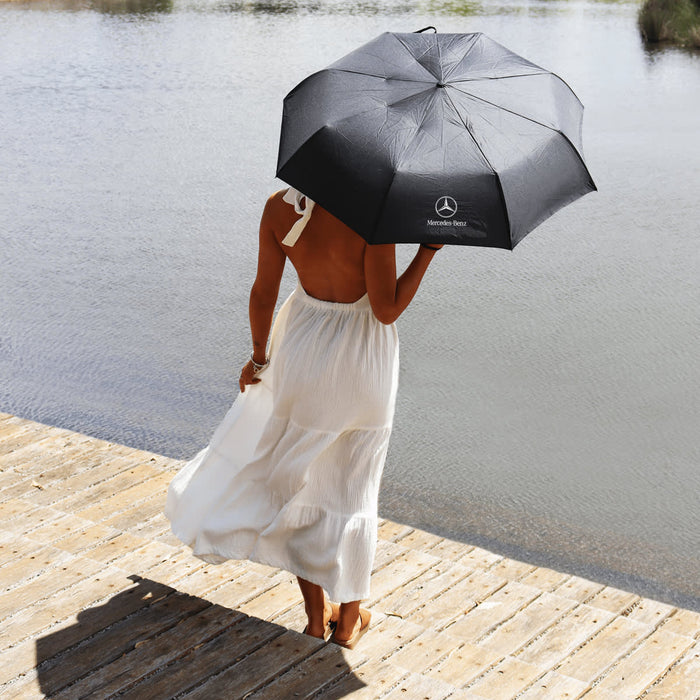 Poppins Umbrella - A black umbrella with a logo, held by a person in a white dress near a water body.