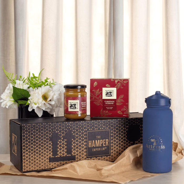 Festive Essentials Set - A blue drink bottle, a jar of jam, a box of biscuits, and a vase of flowers arranged on a decorative box.