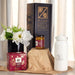 Festive Essentials Set - A white drink bottle, a jar of jam, a floral arrangement, and a decorated box, all presented in a festive setting.