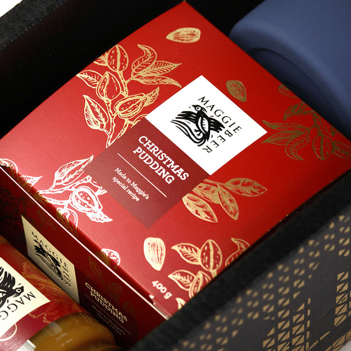 Festive Essentials Set - A festive product set featuring a red box of Christmas pudding, a glass jar, and a blue drink bottle.