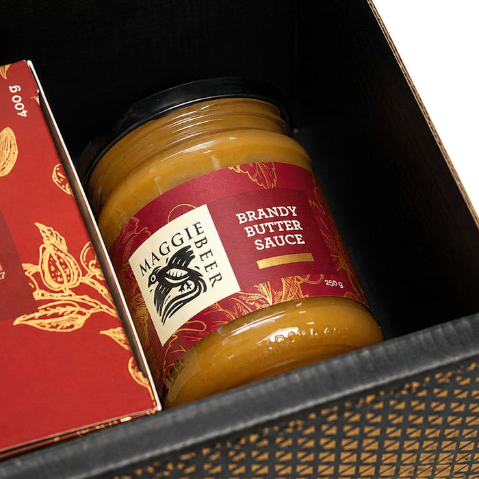 Festive Essentials Set - A jar of brandy butter sauce in a black box, featuring a decorative label and a logo. The sauce is golden in colour.
