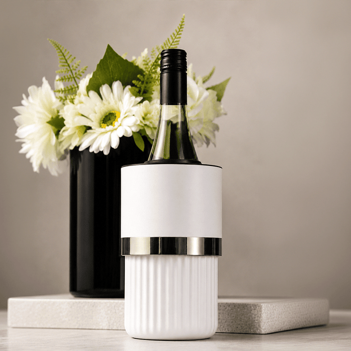 The Entertainer Set - A white wine bottle cooler with a silver band, placed on a marble surface beside a black vase with white flowers.