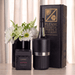 The Entertainer Set - A black wine bottle cooler with silver band, a box of brittle, and a vase with white flowers, arranged on a table.