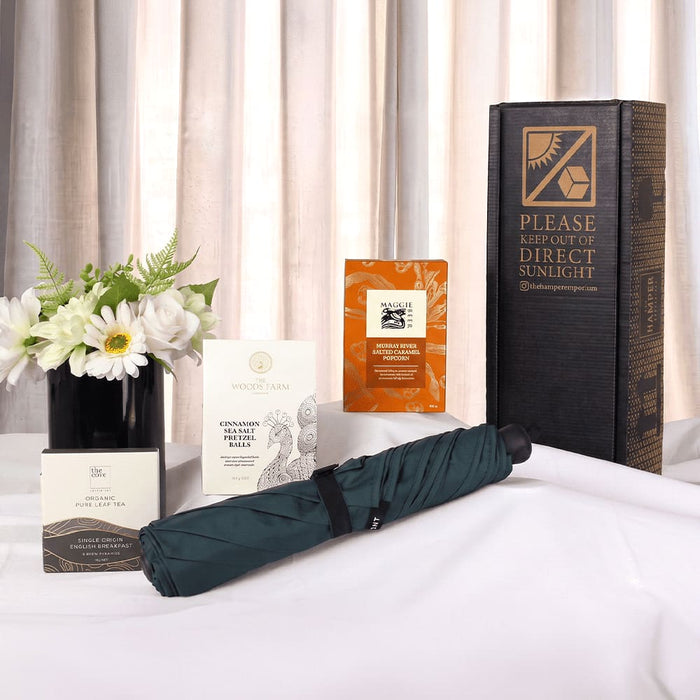 The Blunt Umbrella All Weather Set - A green umbrella set with a box, floral arrangement, and various product boxes displayed on a white surface.