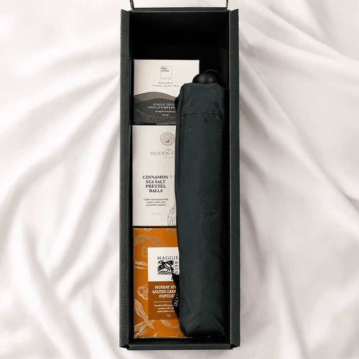The Blunt Umbrella All Weather Set - A black umbrella and snack items in a rectangular box on a soft surface.