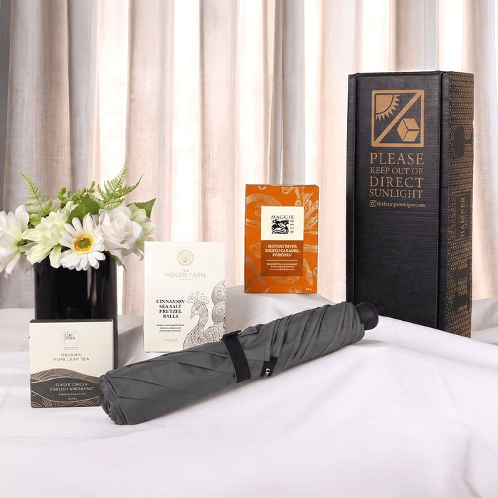 The Blunt Umbrella All Weather Set - A grey umbrella, flower arrangement, and several boxes with a promotional package, all displayed on a white surface.