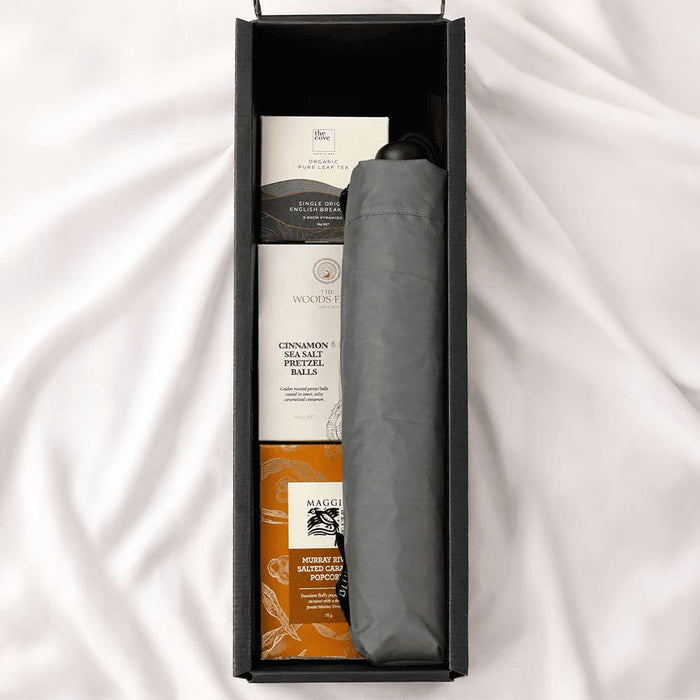 The Blunt Umbrella All Weather Set - A grey umbrella nestled in a black box alongside snack items, including pretzel balls and popcorn.