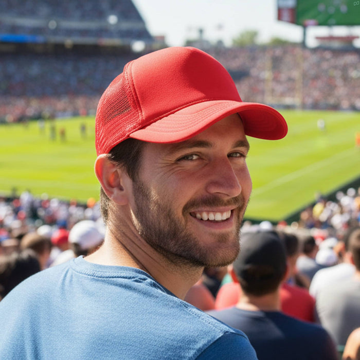 Classic 5 Panel Trucker Mesh Cap - A man wearing a red Classic 5 Panel Trucker Mesh Cap smiles at a sports event, with a crowd in the background.