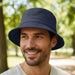 Long Beach Bucket Hat – Large - A navy blue bucket hat displayed on a smiling man, set against a park backdrop with trees. The hat has a logo.