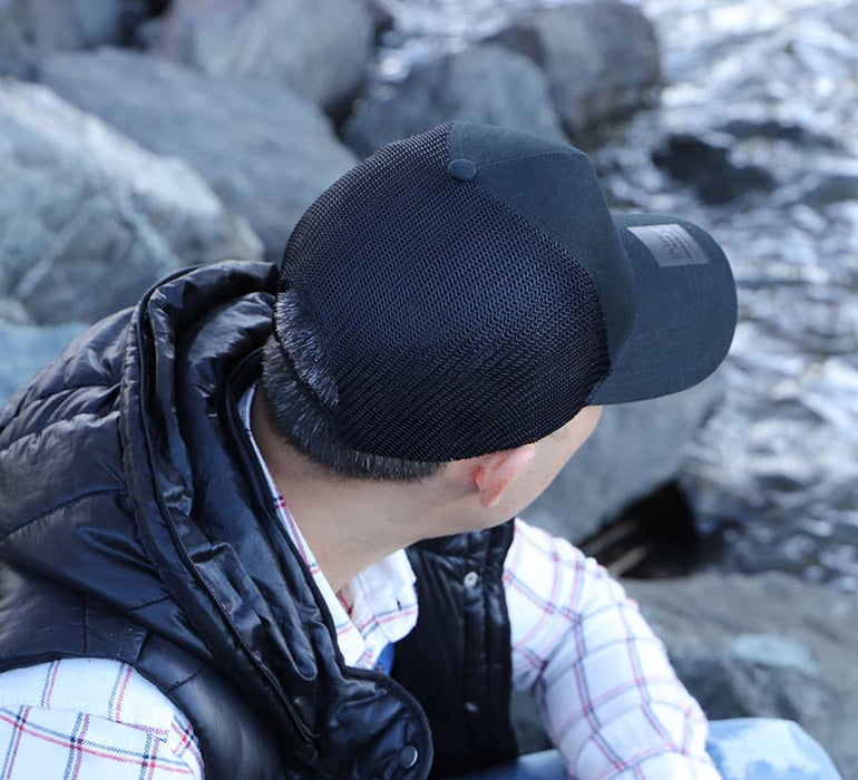 Cotton/Mesh - A black cotton/mesh cap worn by a person seated near rocks, with a reflective body warmer visible.