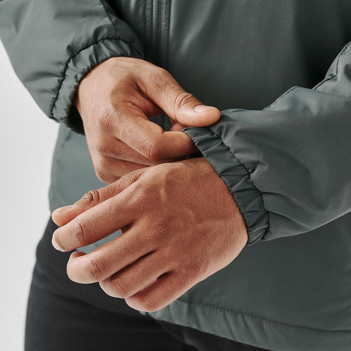 Men's Pacifica Thermal Jacket - A close-up of hands adjusting the elastic cuff of a dark green thermal jacket, featuring a logo.