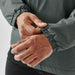 Men's Pacifica Thermal Jacket - A close-up of hands adjusting the elastic cuff of a dark green thermal jacket, featuring a logo.