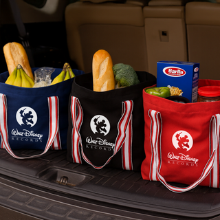 Century Canvas Tote Bag - Three canvas tote bags in red, black, and blue, filled with groceries like bread, vegetables, and pasta. Each bag has a logo.