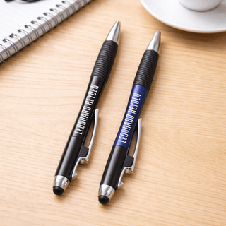 The Ironhide Pen - A pair of pens, one black and one blue, with grips, resting on a wooden surface near a cup and notebook.