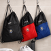 The Buddy Drawstring Bag - Three drawstring bags hang on hooks; one black, one red, and one blue, each featuring a logo and zip pocket.