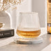 Velora Tumbler Gift Set by The Line Edit. - A drink bottle with a ribbed clear glass design sits on a marble coaster, featuring a golden liquid inside.