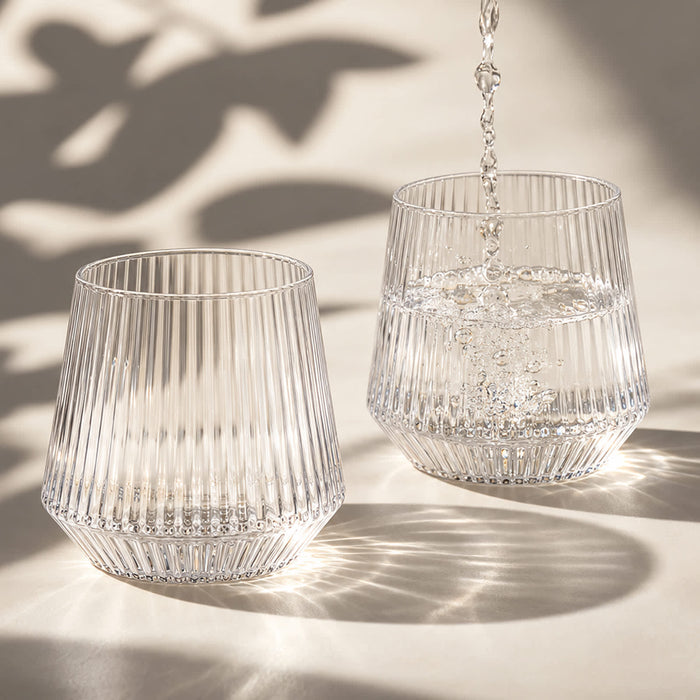 Velora Tumbler Gift Set by The Line Edit. - A drink bottle featuring a ribbed design, made of clear glass, with water being poured into two glasses.