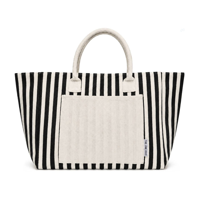 The Weekend Edit - A striped tote bag in black and white with a plain cream-coloured front pocket and handles. It has a logo.