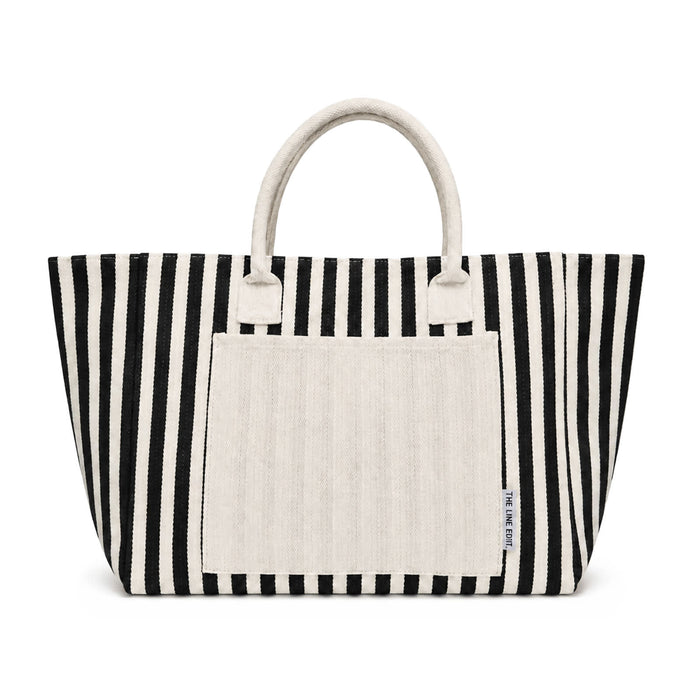 Hampton Tote Bag by The Line Edit. - A striped tote bag in black and white with a plain cream-coloured front pocket and handles. It has a logo.