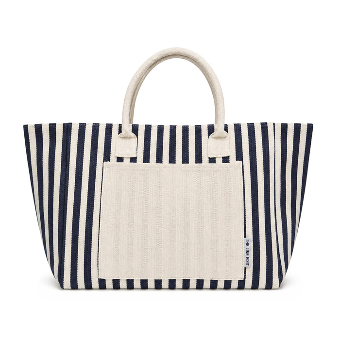 Hampton Tote Bag by The Line Edit. - A navy and cream striped tote bag with two sturdy handles and a front pocket. It features a branding logo.